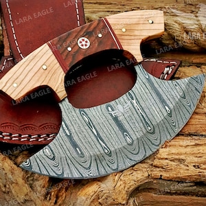 Op de afbeelding: Een handgesmeed Damascus stalen bijl met een houten handvat. De bijl heeft een uniek, gepatenteerd blad en een leren schede.