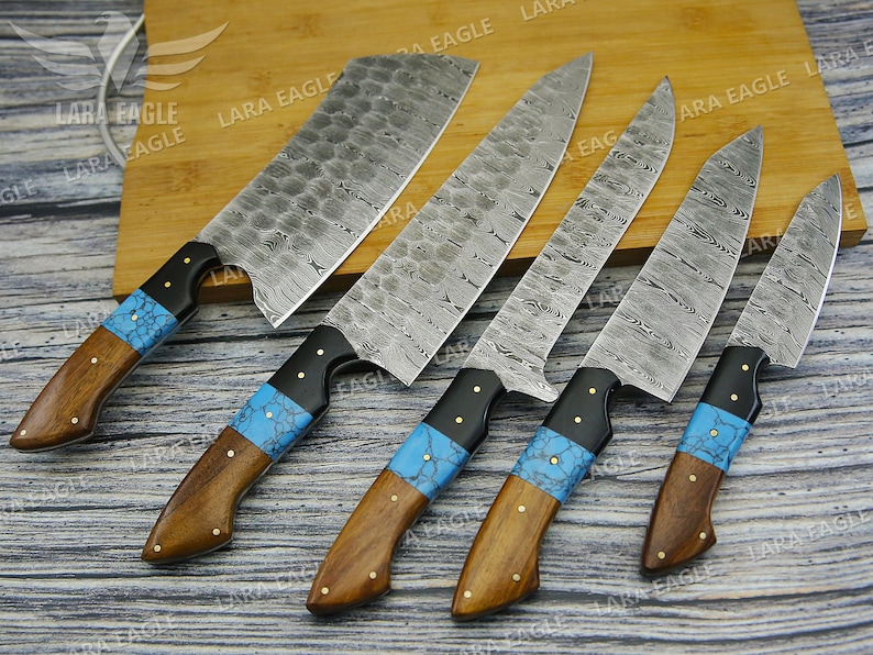 May include: Five kitchen knives with blue and black handles and Damascus steel blades. The knives are arranged on a wooden cutting board.