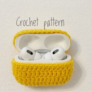 Könnte beinhalten: Eine gelbe, gehäkelte Hülle für kabellose Ohrhörer, mit dem Text "Crochet pattern" darüber. Die Hülle ist geöffnet und zeigt weiße Ohrhörer. Die Hülle besteht aus strukturiertem, gelbem Garn.