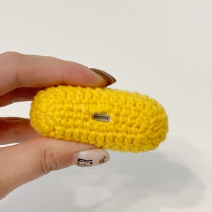 May include: A bright yellow, crocheted case, likely for earbuds or a small electronic device. The case is rectangular with rounded edges and a small opening on one side. The crochet work is tight and even, giving the case a textured appearance.