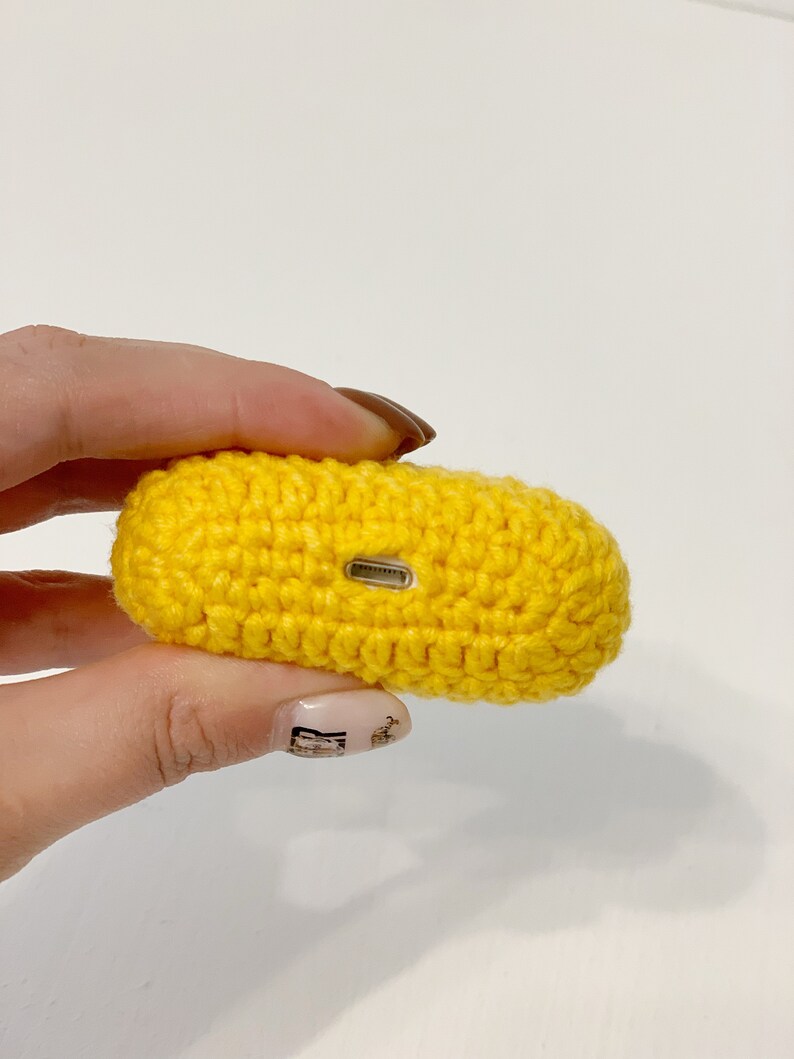 May include: A bright yellow, crocheted case, likely for earbuds or a small electronic device. The case is rectangular with rounded edges and a small opening on one side. The crochet work is tight and even, giving the case a textured appearance.