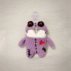 May include: Purple crocheted amigurumi doll with black eyes, a red heart, and black stitching. The doll is designed to hold a pair of wireless earbuds. The text "CROCHET pattern" is written above the doll.