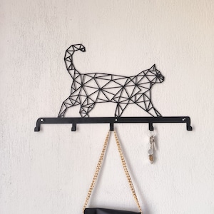 May include: Black metal geometric cat wall hook with five hooks and a gold chain hanging from one of the hooks.