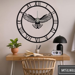 Peut inclure: Horloge murale en métal noir avec des chiffres romains et une silhouette d'oiseau aux ailes déployées. L'horloge est montée sur un mur blanc au-dessus d'un bureau en bois avec une plante en pot, des livres et une lampe.