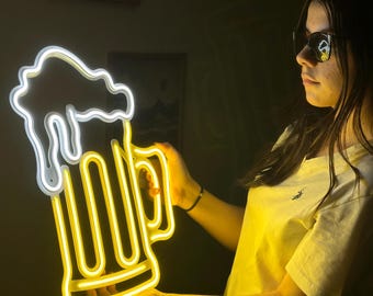 May include: A neon sign shaped like a beer mug with a white outline and a yellow glow. The sign is being held by a person wearing a yellow shirt.