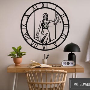 Könnte beinhalten: Schwarze Wanduhr aus Metall mit römischer Ziffernblatt-Gestaltung. Die Uhr zeigt eine Silhouette einer Figur, die eine Justizwage und ein Schwert hält. Die Uhr ist an einer weißen Wand über einem Holztisch mit einer Topfpflanze, Büchern und einer Lampe angebracht.
