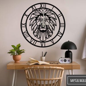 Pode incluir: Relógio de parede de metal preto com um design de leão geométrico. O relógio está pendurado em uma parede branca acima de uma mesa de madeira com uma planta, livros e uma lâmpada.