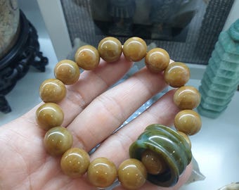 Op de afbeelding: Een jade armband met een groene jade hanger. De armband is gemaakt van ronde, geelbruine jade kralen.