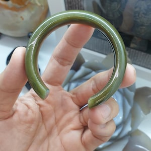 Könnte beinhalten: Ein grünes Jade-Armband. Das Armband ist glatt und poliert, mit einer leicht abgerundeten Form.