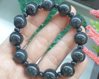 May include: A stretch bracelet featuring large, smooth, dark gray spherical beads alternating with smaller, round, dark gray spacer beads. The beads have a polished, reflective surface and are arranged in a circular pattern on an elastic cord.