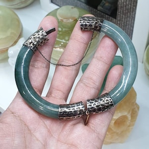 Può includere: Un braccialetto di giada verde con chiusure in metallo martellato argentato. Il braccialetto è aperto e le chiusure sono visibili.