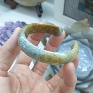 May include: A jade bangle bracelet with a green and brown color scheme. The bracelet is smooth and polished.