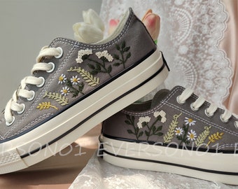 May include: A pair of gray canvas sneakers with white soles and embroidered floral designs in shades of green, yellow, and white.