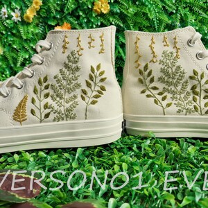 May include: A pair of white high-top canvas shoes with green and yellow embroidered floral designs.