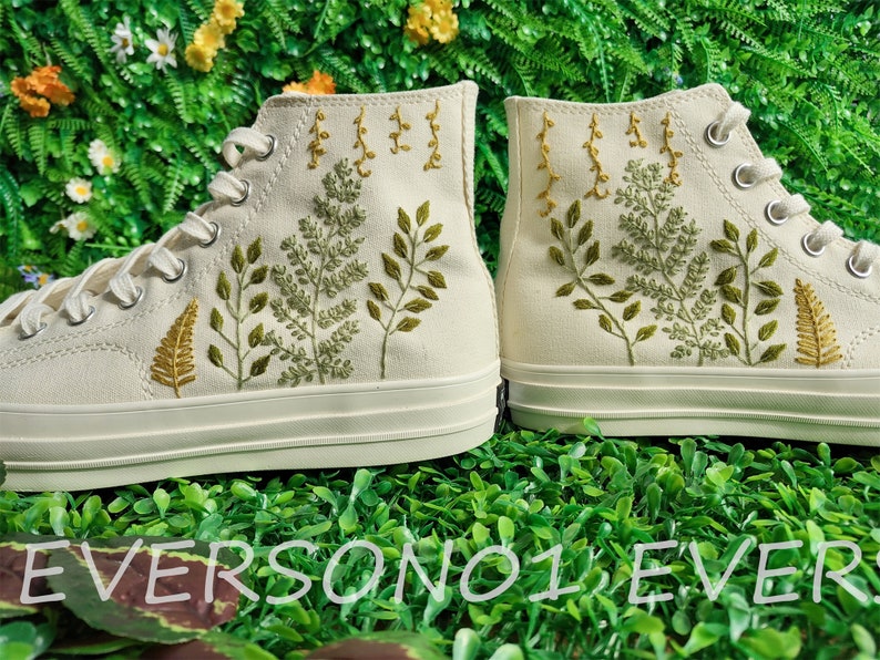 May include: A pair of white high-top canvas shoes with green and yellow embroidered floral designs.