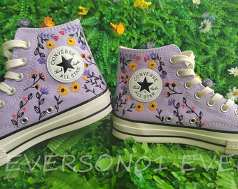 May include: Purple high-top Converse sneakers with embroidered flowers and vines. The Converse All Star logo is visible on the side of the shoe.