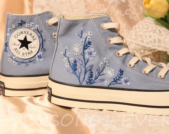 Könnte beinhalten: Ein Paar hellblaue High-Top-Sneaker mit weißen Schnürsenkeln und einer weißen Gummisohle. Die Sneaker sind mit einem floralen Muster in Blau- und Weißtönen bestickt. Der linke Sneaker hat einen Converse All Star-Logopatch.