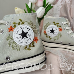 May include: A pair of light green high-top Converse sneakers with embroidered floral details and the text "Converse Chuck Taylor All Star" on the side.