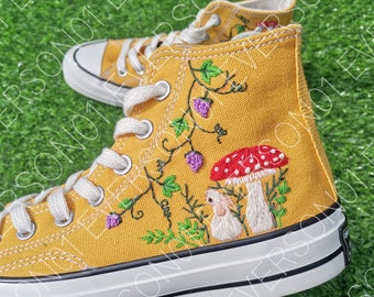 May include: Yellow high-top canvas sneakers with embroidered mushrooms, vines, and berries. The sneakers have white laces and a white rubber sole.