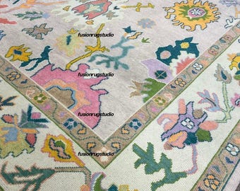 Può includere: Un grande tappeto rettangolare con sfondo beige e un colorato motivo floreale. Il tappeto presenta un bordo con un motivo geometrico ripetuto e il testo "fusionrugstudio" in più punti.