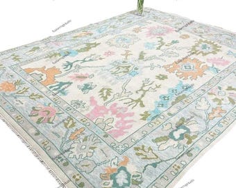 Può includere: Un tappeto rettangolare con un motivo floreale in colori pastello. Il tappeto presenta uno sfondo color crema con disegni floreali rosa, blu e arancioni. Un vaso di fiori è posto sul tappeto.