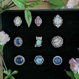 Könnte beinhalten: Eine schwarze Samt-Präsentationsbox mit 10 silbernen Ringen mit verschiedenen farbigen Glassteinen. Die Ringe sind in einem Gittermuster angeordnet.