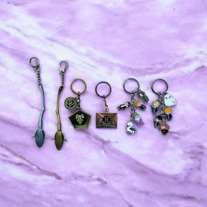 Könnte beinhalten: Sechs Harry-Potter-Schlüsselanhänger mit verschiedenen Anhängern. Die Anhänger umfassen einen Besen, einen Hogwarts-Brief, einen goldenen Schnatz und eine Gruppe von Harry-Potter-Charakteren.