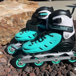 Könnte beinhalten: Paar Inline-Skates mit türkisfarbenen und schwarzen Akzenten. Die Skates haben ein weißes und schwarzes Schuhdesign mit türkisfarbenen Rollen und einem silbernen Rahmen. Die Skates sind für den Freizeitgebrauch konzipiert.