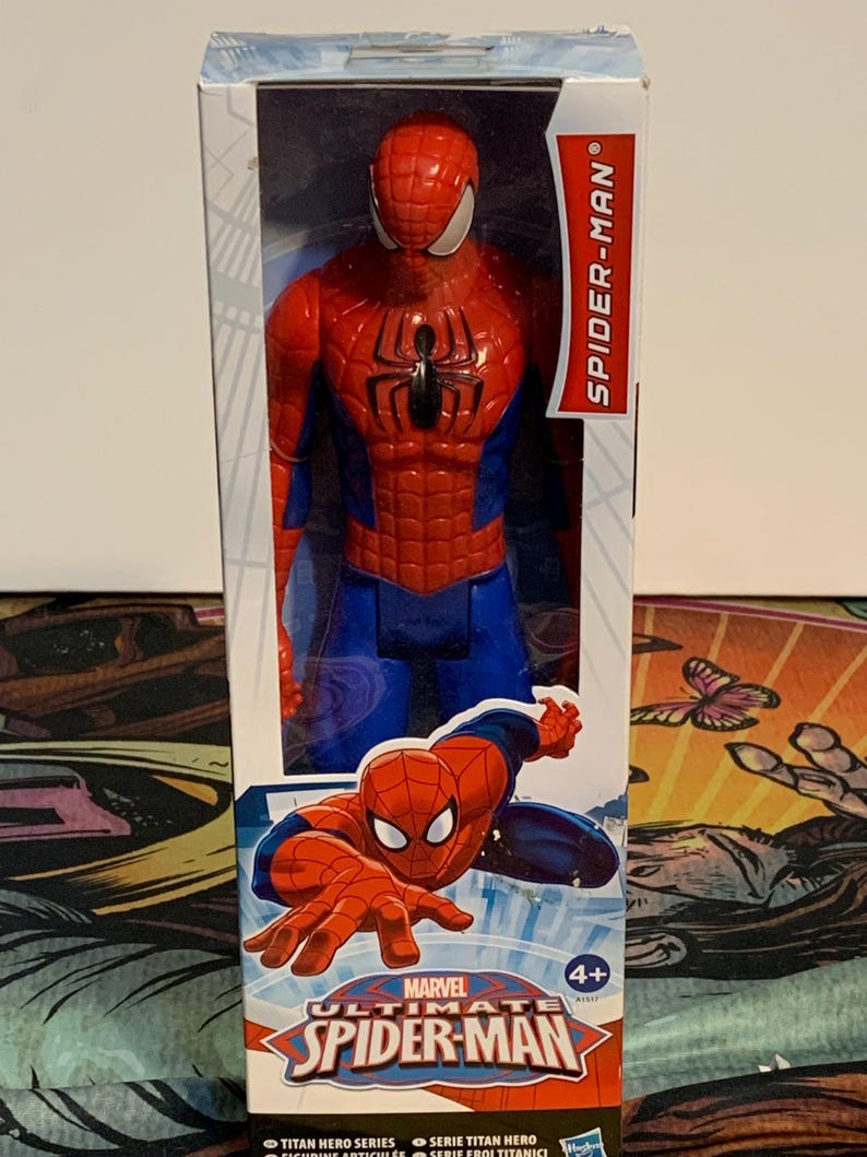 May include: A red and blue action figure of Spider-Man in a box. The box has the words "Marvel Ultimate Spider-Man" on it. The figure is posed in a dynamic action pose. The box is labeled 4+.