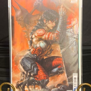 May include: A comic book cover featuring Wonder Woman in a dynamic pose, with Batman in the background. The artwork showcases a vibrant color palette with red and orange hues. The comic is titled "Wonder Woman" and has the DC Comics logo.