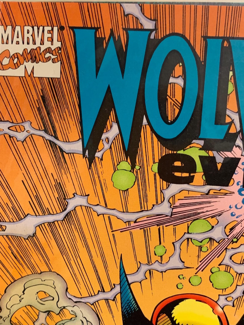 Pu&ograve; includere: Copertina di fumetto con il logo Marvel Comics e la parola "WOLVERINE" in grandi lettere blu. Lo sfondo &egrave; arancione con linee nere che si irradiano verso l'esterno ed elementi grafici verdi e bianchi.