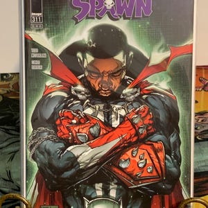 Könnte beinhalten: Spawn Comic-Cover, Ausgabe 311, mit einem Porträt einer Person in einem Kostüm mit roten und weißen Akzenten. Das Cover enthält den Text "IN MEMORY OF CHADWICK BOSEMAN (1976-2020)" und das Spawn-Logo.