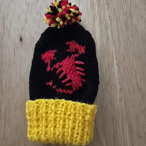 May include: Black knitted hat with a red and yellow embroidered design and a yellow pom-pom on top.