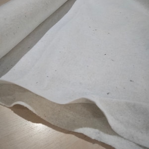 Può includere: Imbottitura in cotone bianco, un materiale morbido e soffice utilizzato per la trapunta e l'artigianato. È arrotolata e piegata, mostrando la sua consistenza e spessore.