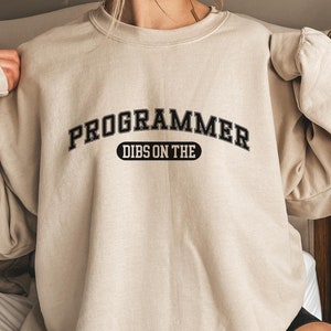 May include: A beige sweatshirt with the text "PROGRAMMER DIBS ON THE" in black lettering. The text is in a collegiate font.