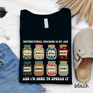 Könnte beinhalten: Schwarzes T-Shirt mit dem Text "INSTRUCTIONAL COACHING IS MY JAM" und "AND I'M HERE TO SPREAD IT". Das Shirt zeigt Gläser mit den Aufschriften "Guide", "Inspire", "Grow", "Model", "Reflect", "Coach", "Support" und "Empower".