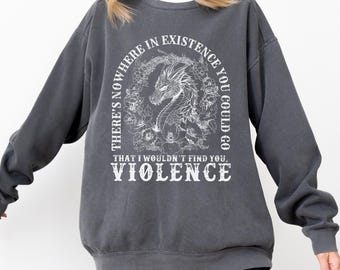 Può includere: Felpa grigio scuro con testo bianco e un'illustrazione di un drago. Il testo recita: "THERE'S NOWHERE IN EXISTENCE YOU COULD GO THAT I WOULDN'T FIND YOU, VIOLENCE". Il drago è circondato da elementi floreali.