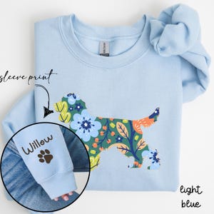Peut inclure: Sweat-shirt bleu clair avec une silhouette de chien à motif floral sur le devant et le mot "Willow" et une empreinte de patte sur la manche.