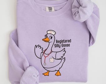 May include: A purple sweatshirt with a cartoon goose wearing a nurse's hat and a stethoscope. The text "Registered Silly Goose" is printed on the sweatshirt.