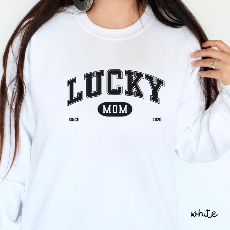 以下が含まれることがあります： 白いスウェットシャツに、黒い文字で「Lucky Mom Since 2020」と書いてあります。