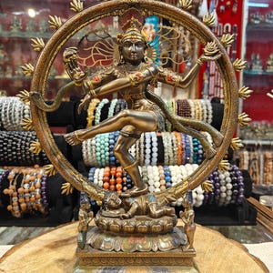 Könnte beinhalten: Eine Bronzestatue der hinduistischen Gottheit Shiva Nataraja, des Herrn des Tanzes, in einer dynamischen Pose in einem kreisförmigen Rahmen. Die Statue weist komplizierte Details auf, darunter mehrere Arme, Schmuck und eine Schlange. Der Sockel zeigt eine liegende Figur.
