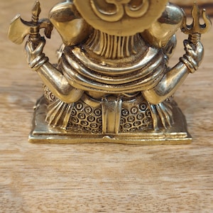 May include: A detailed brass statue of a deity, featuring multiple arms holding various objects. The statue has a prominent headpiece with a symbol and is set on a decorative base. The overall design is intricate and ornate, with a polished finish.
