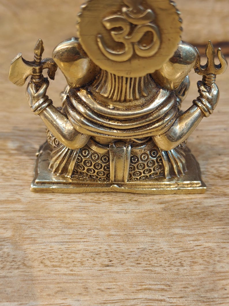 May include: A detailed brass statue of a deity, featuring multiple arms holding various objects. The statue has a prominent headpiece with a symbol and is set on a decorative base. The overall design is intricate and ornate, with a polished finish.