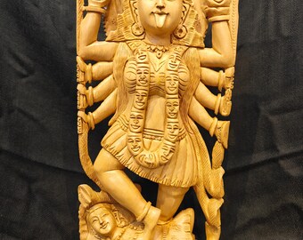 Può includere: Statua in legno intagliato di una divinità con molte braccia, con una corona e una ghirlanda di volti. La figura è in piedi su un'altra figura reclinata. La statua è di colore marrone chiaro e presenta dettagli intricati.
