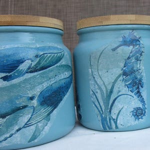 Peut inclure: Trois bocaux en céramique bleu clair avec des couvercles en bois. Chaque bocal présente un motif de vie marine différent : des baleines, un hippocampe et une tortue de mer. Les bocaux sont décorés avec une technique de découpage.