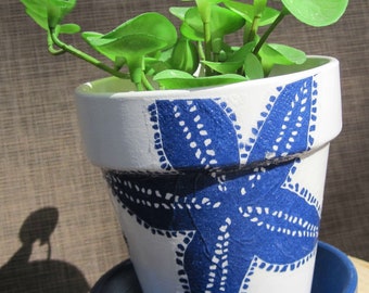 Può includere: Vaso in ceramica bianca con un design a stella marina blu. Il vaso è pieno di piante verdi.