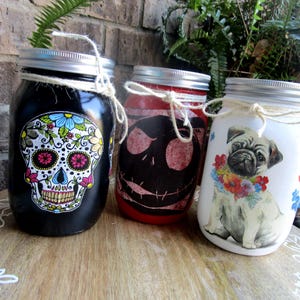 Pu&ograve; includere: Tre barattoli di vetro decorati con diversi disegni. Il primo barattolo &egrave; nero con un disegno di teschio di zucchero colorato. Il secondo barattolo &egrave; rosso con un disegno di Jack Skellington in bianco e nero. Il terzo barattolo &egrave; bianco con un carlino che indossa una ghirlanda di fiori.