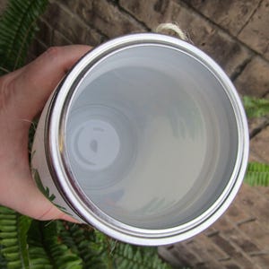 Pu&ograve; includere: Una lattina di metallo bianca con un coperchio argentato. La lattina ha un disegno floreale verde e bianco. Il coperchio &egrave; aperto e l'interno della lattina &egrave; visibile.