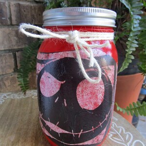 Pu&ograve; includere: Un barattolo di vetro rosso con un coperchio argentato e un fiocco di spago bianco. Il barattolo &egrave; decorato con un'immagine in nero e rosso di Jack Skellington de The Nightmare Before Christmas.