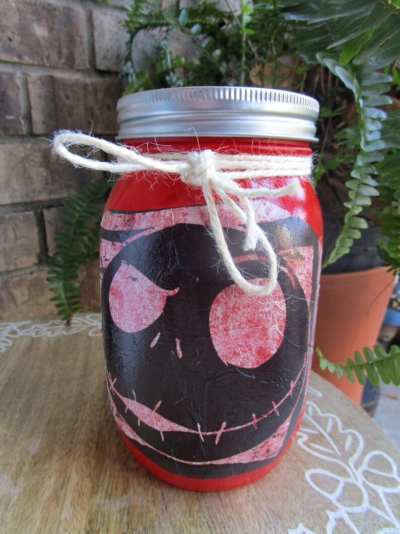 Pu&ograve; includere: Un barattolo di vetro rosso con un coperchio argentato e un fiocco di spago bianco. Il barattolo &egrave; decorato con un'immagine in nero e rosso di Jack Skellington de The Nightmare Before Christmas.